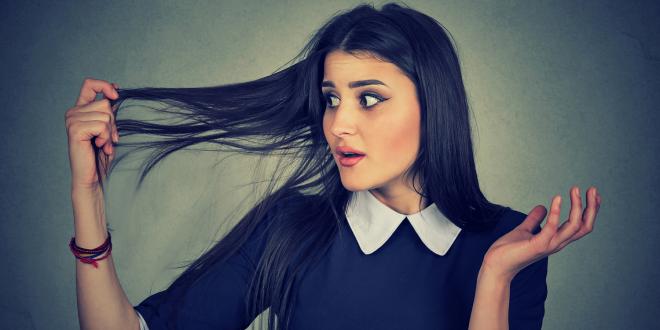 A surprised young woman holding her thinning hair