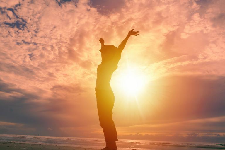 Happy woman raising hands up and beautiful sunrise in background.